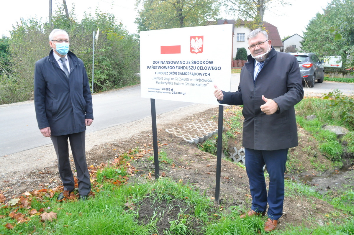 Burmistrz Kartuz i Jego Zastępca. W środku tablica informacyjne dot. dofinansowania przebudowy drogi w Pomieczyńskiej Hucie.