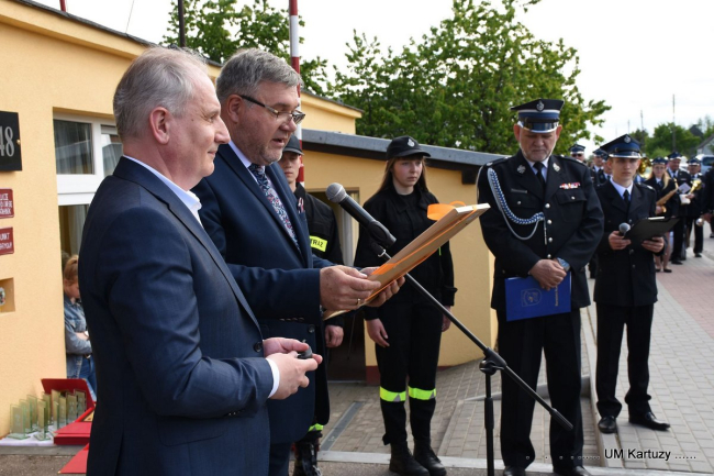 Grafika przedstawia przekazanie wozy ratowniczo-gaśniczego przez Burmistrza Kartuz